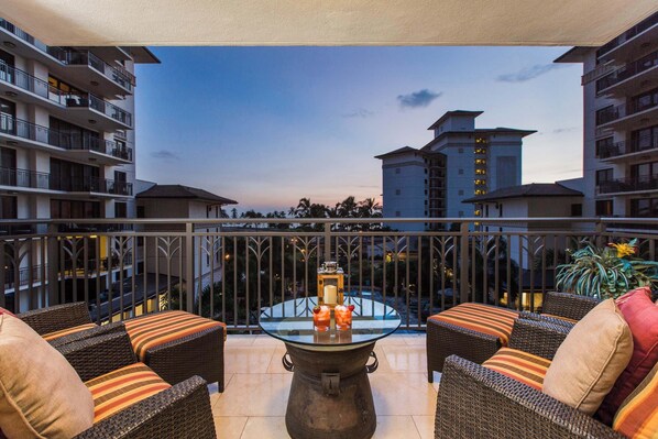 A balcony with wicker furniture, a glass table, and a view of surrounding buildings. - Hale Hauoli Ko Olina Villa w/ Beach & Pool! (Kapolei)