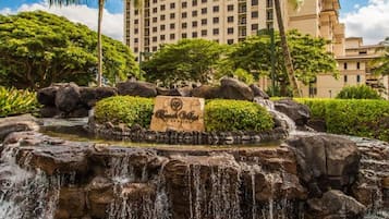 A hotel with a large building, a waterfall, and palm trees.