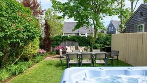 A backyard with a hot tub, a wooden fence, and a patio with outdoor furniture. - Historic Nantucket Home | Hot Tub & Downtown Steps (Nantucket)