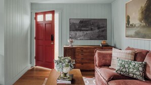 Un salon avec une porte rouge, un meuble en bois, un canapé marron et un tableau accroché au mur.