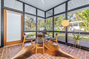 A room with a glass door, a round table with chairs, a cowhide rug, and a view of greenery outside. - Mid Century Modern Weekly Winter Rates! (Tampa)