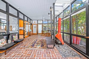 A spacious indoor area with a brick floor, a colorful rug, and a seating area with cushions and a table. - Mid Century Modern Weekly Winter Rates! (Tampa)
