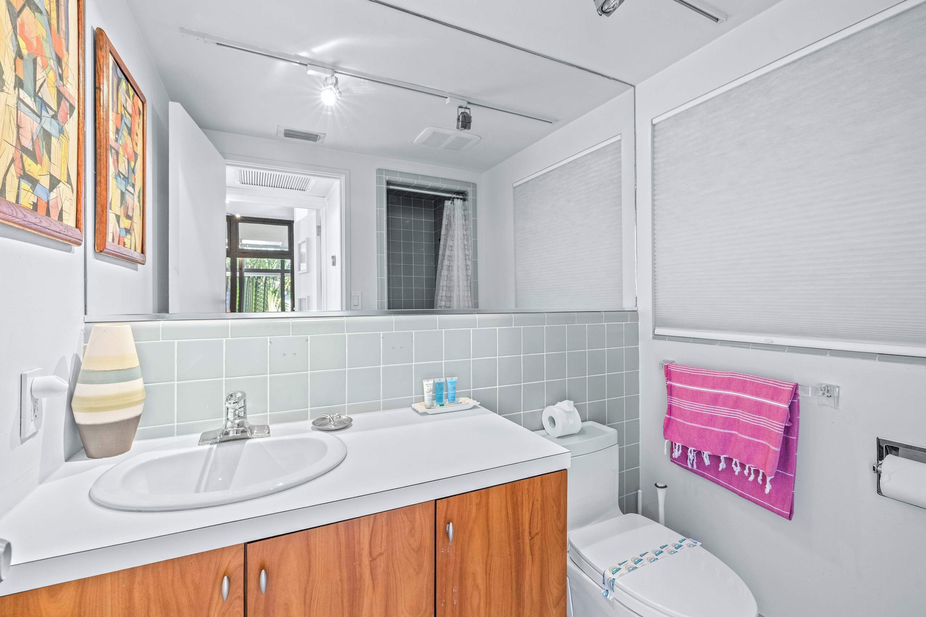 Un baño con lavamanos blanco, tocador de madera, espejo, toallero y un inodoro.