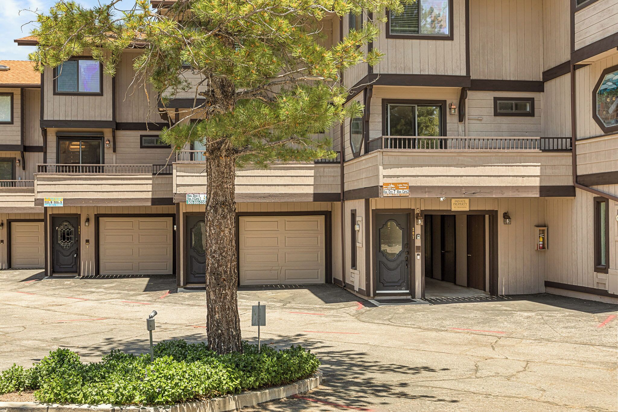 A multi-story residential building with a central entrance, garage doors, and a small tree in the foreground.