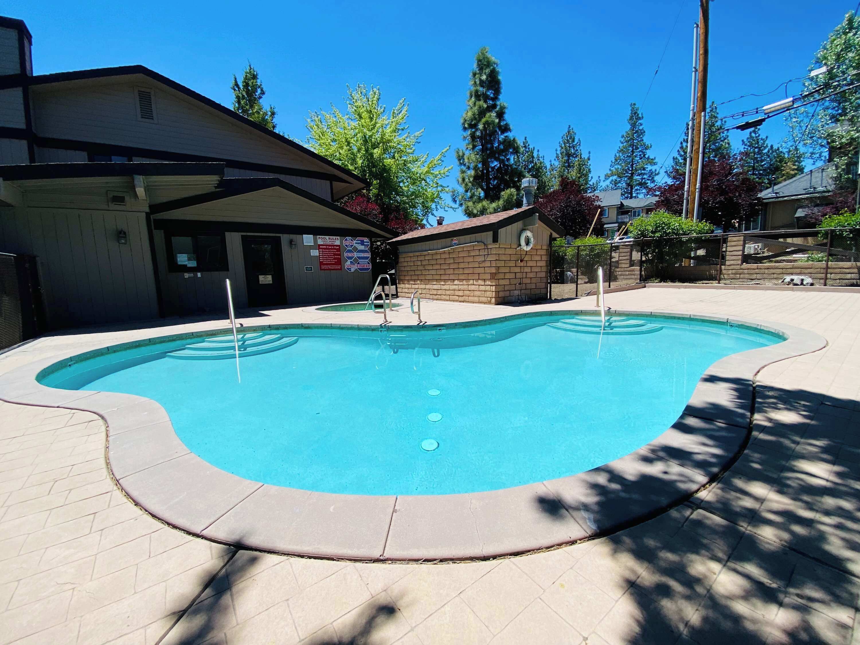 A swimming pool with a tiled deck, surrounded by trees and buildings.