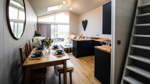 Un comedor con una mesa de madera para cuatro personas, un espejo en la pared y un adorno con forma de corazón sobre la encimera de la cocina.
