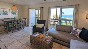 A spacious living area with a dining table, a sofa, and a balcony with a view of the ocean.