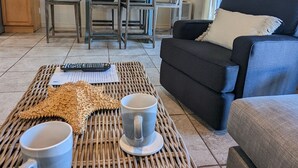 A living room with a sofa, two chairs, a dining table, and a coffee table with two mugs and a decorative item.