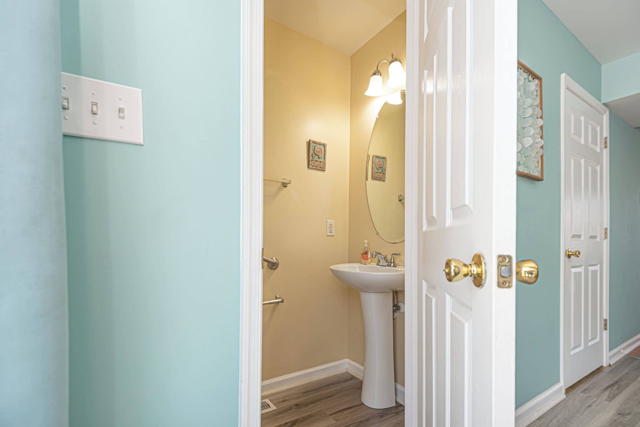 Une salle de bain avec un lavabo sur colonne, un miroir et une porte dotée d’une poignée en laiton.