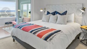 Un dormitorio moderno con una cama grande, un ventilador de techo y vista a la playa a través de una puerta corrediza.