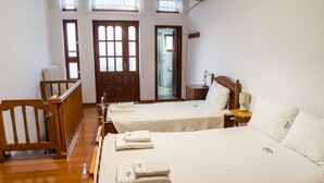 A hotel room with two beds, wooden furniture, and a view of the hallway. - Thòlos Home (Αρχοντική)