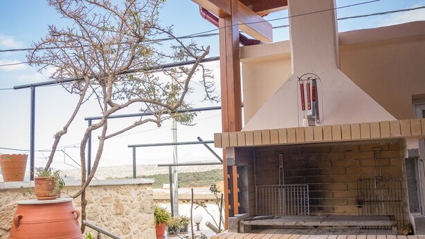 An outdoor patio with a brick fireplace, terracotta pots, and a tree. - Thòlos Home (Αρχοντική)