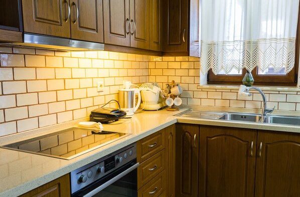 Una cocina con armarios de madera, un lavamanos de acero inoxidable y una ventana con cortinas de encaje.