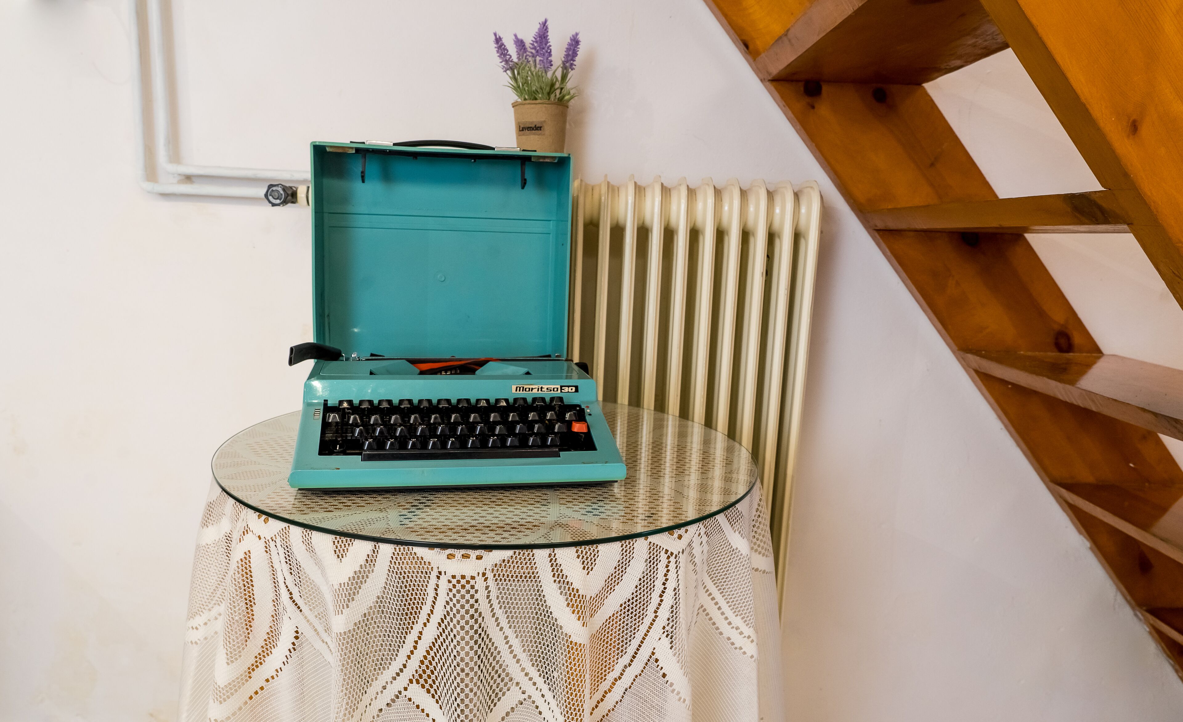 Une machine à écrire turquoise posée sur une table en verre recouverte d’une nappe en dentelle blanche.