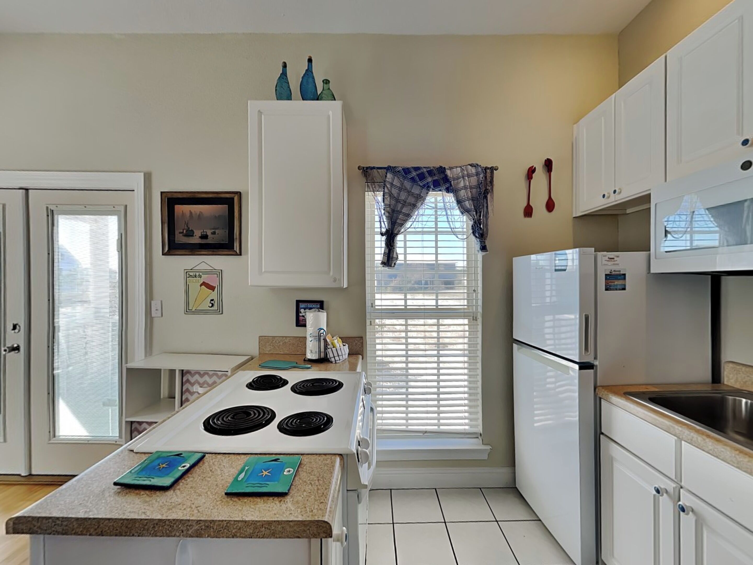 Una cocina con armarios blancos, estufa, refrigerador y ventana con persianas.