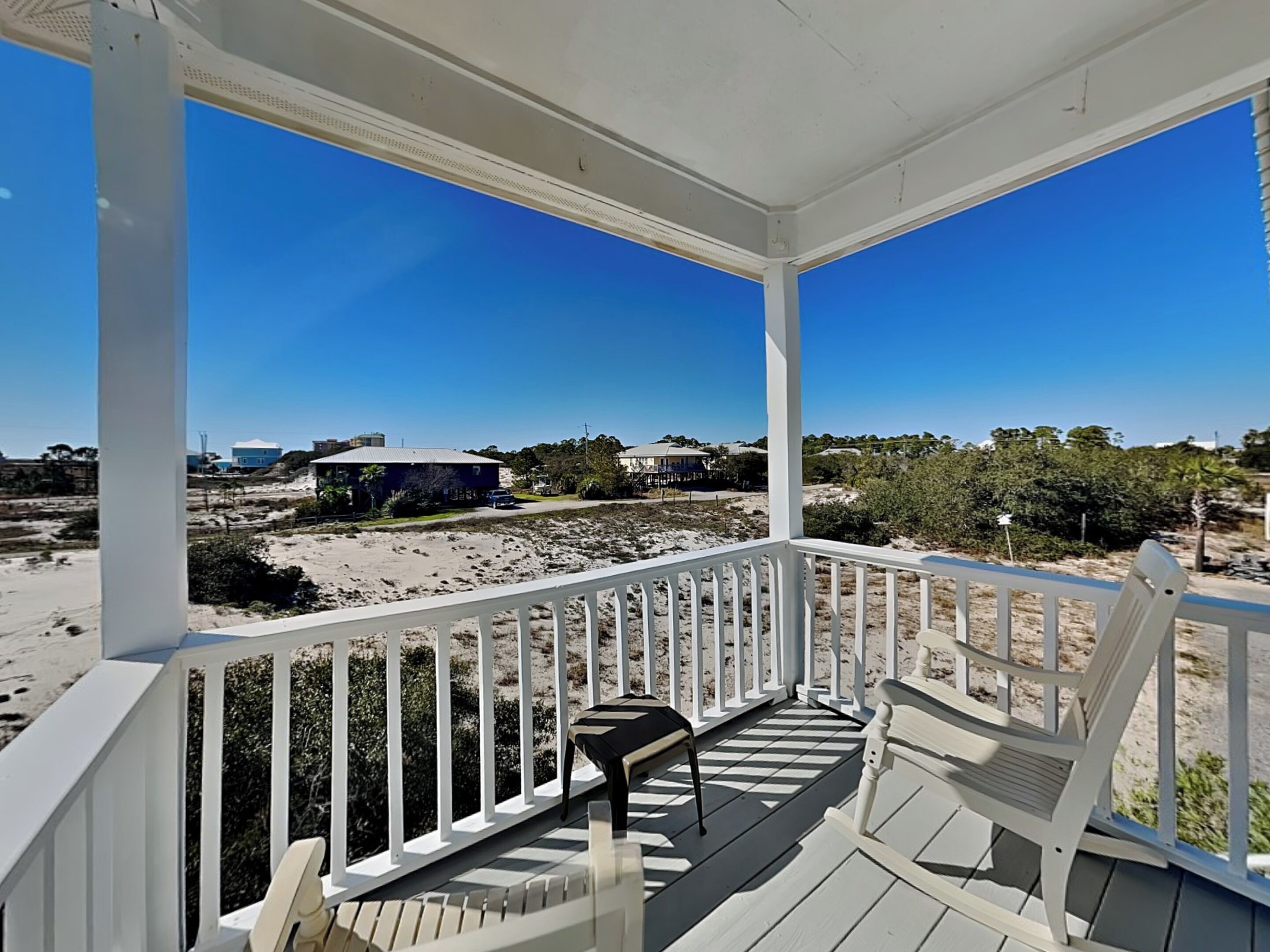 A covered porch with a view of the beach and houses in the distance.