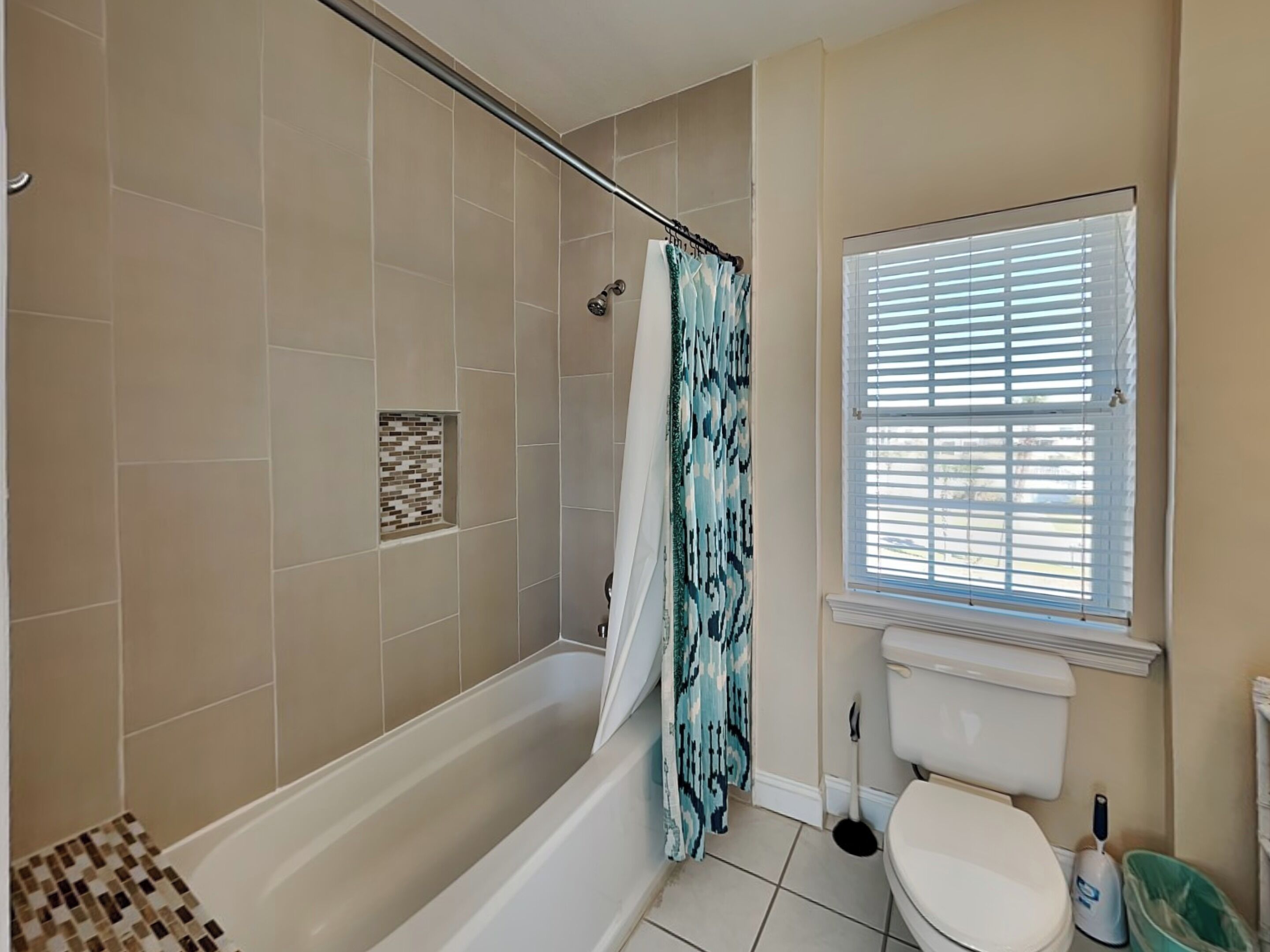 A bathroom with a shower, toilet, and a window with blinds.