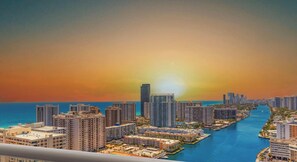 A coastal cityscape with high-rise buildings, a marina, and a sunset.