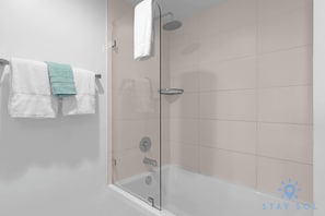 A modern bathroom with a glass shower enclosure, a white bathtub, and a towel rack with two towels.
