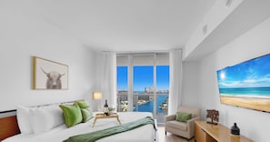 Een moderne hotelkamer met een groot bed, uitzicht op de stad en uitzicht op het strand, plus een ingelijste afbeelding.