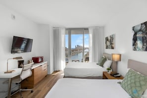 Ein Hotelzimmer mit Bett, Schreibtisch, Stuhl, Fernseher, einem Fenster mit Vorhängen und Bildern an der Wand.