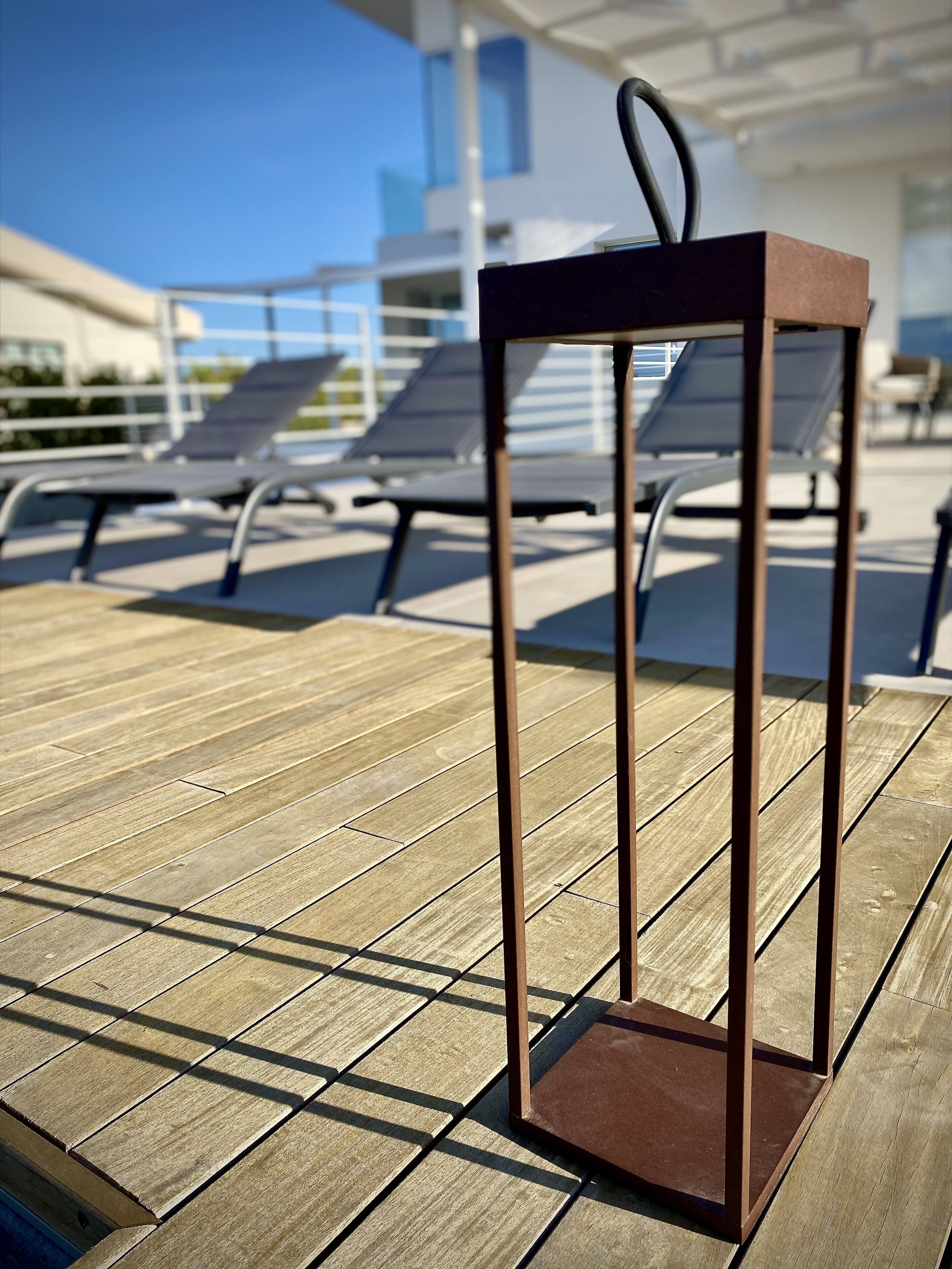 A metal lantern on a wooden deck with lounge chairs in the background.