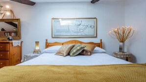 Een slaapkamer met een bed, houten hoofdbord, een ingelijst architectuurtekening aan de muur, een nachtkastje met een lamp, en een kleine tafel met een bloevas.