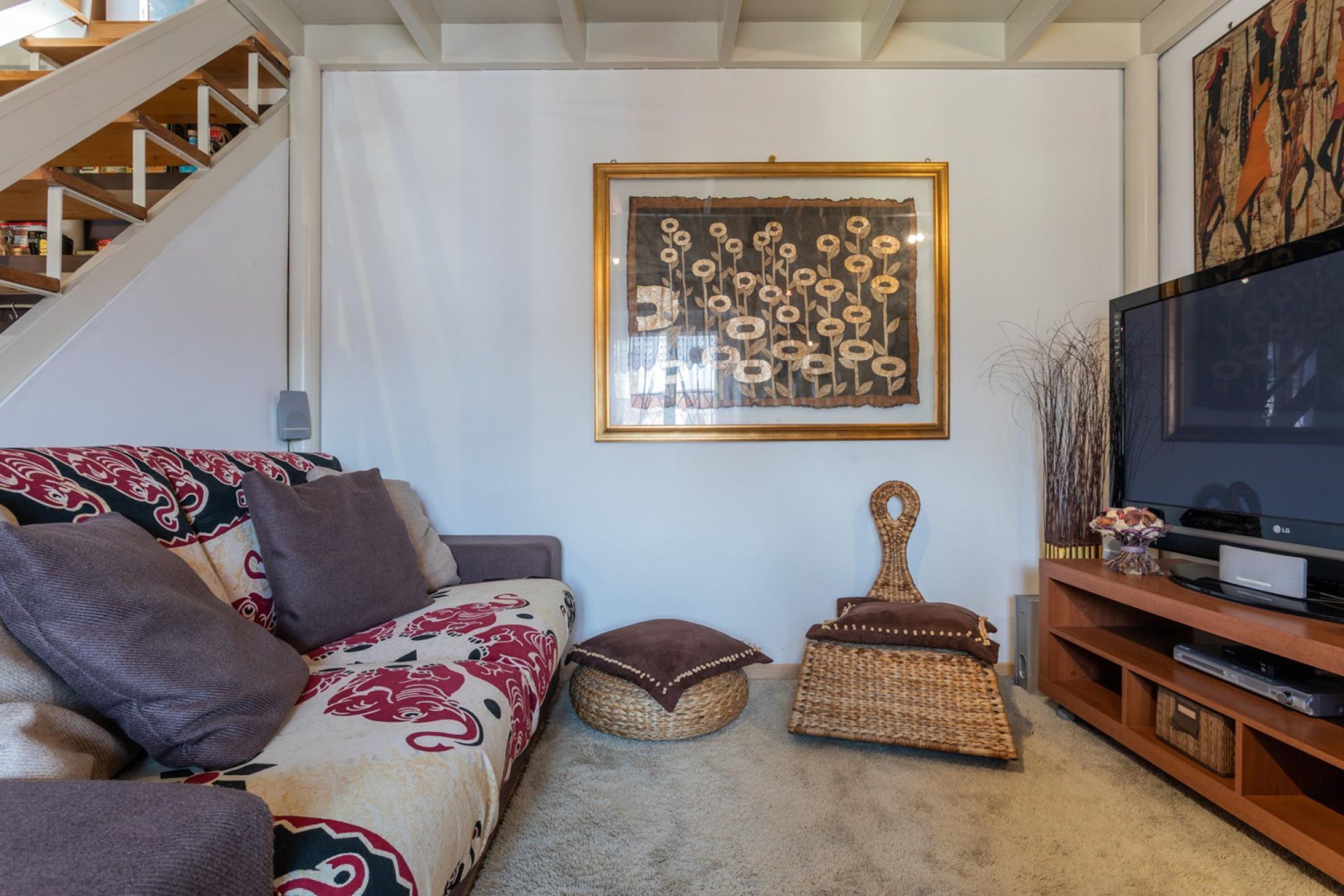 Ein Wohnzimmer mit einer Couch, einem Fernseher, einem gerahmten Kunstwerk und einer Treppe.