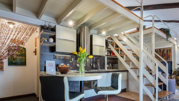Een moderne keuken met een centraal eiland, een trap en een eethoek met een tafel en stoelen.