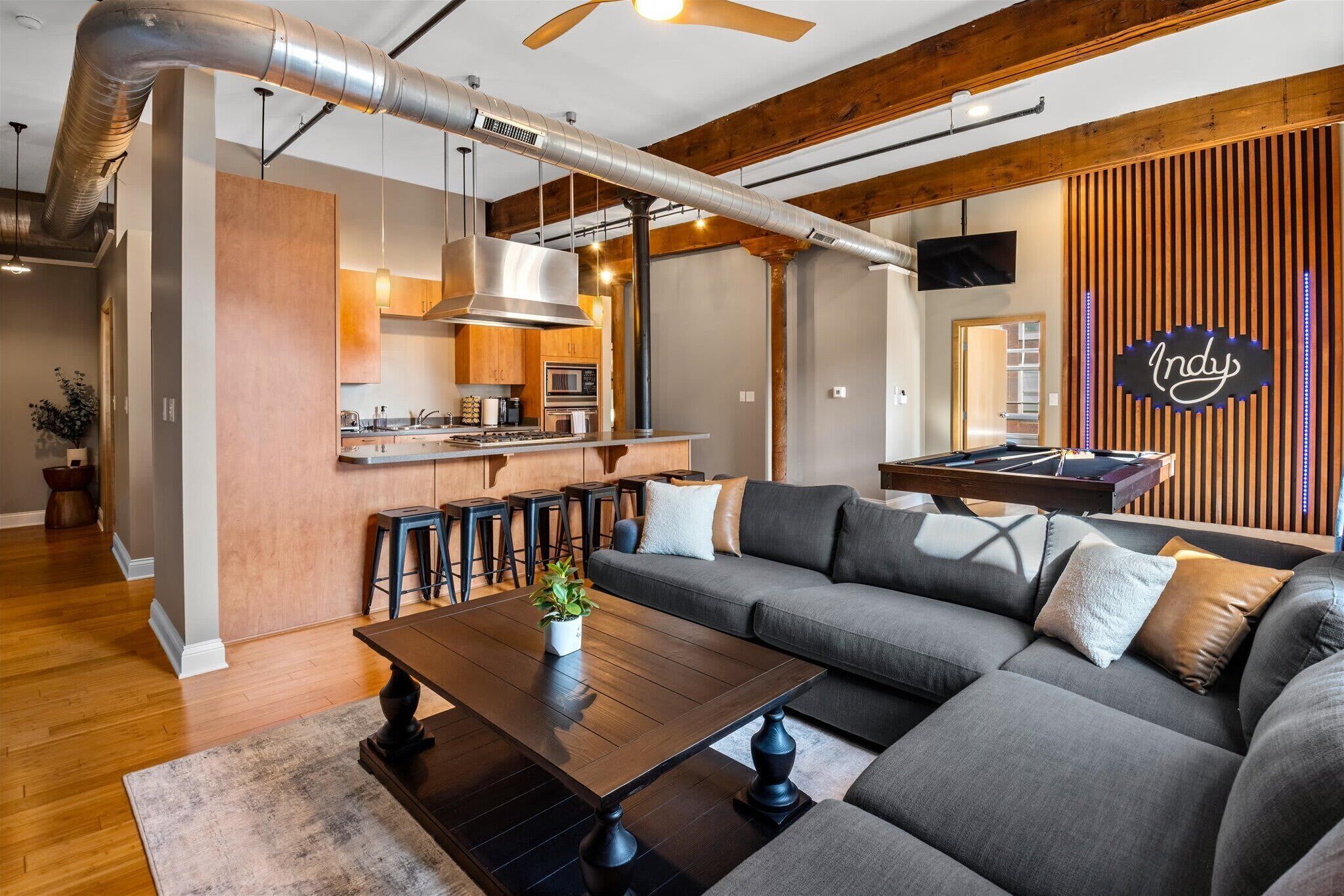 Une cuisine moderne dotée d’un îlot central, un coin repas avec un canapé et une table basse, et un salon avec un grand canapé d’angle.