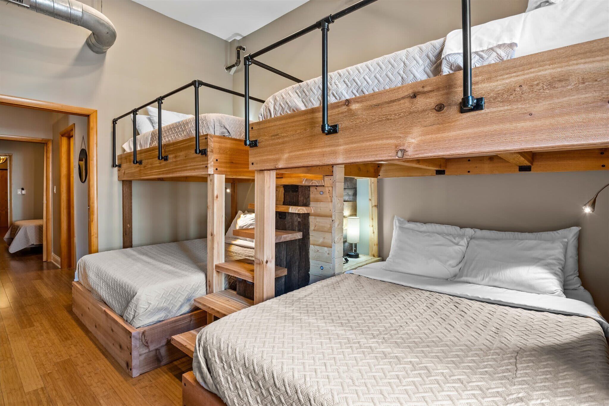 Une chambre avec un lit superposé, un plancher en bois, un escalier et une table de chevet avec une lampe.