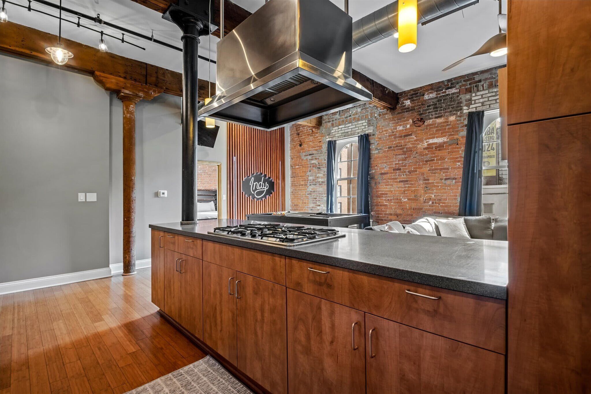 Une cuisine moderne dotée d’un îlot central, de meubles en bois, d’une hotte en acier inoxydable et d’un mur en briques.