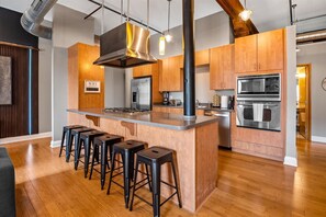 A modern kitchen with a central island, bar stools, stainless steel appliances, and exposed ductwork. - New Loft Near Convention Center (Indianapolis)