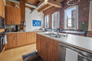 Eine moderne Küche mit Holzausstattung, einer großen Kochinsel mit Spüle und Blick auf ein Backsteinhaus durch große Fenster.