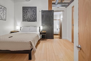 Quarto com cama, mesas de cabeceira, um mapa na parede e uma porta que dá para outro cômodo.