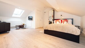 A modern bedroom with a skylight, a large bed, a TV, and a black nightstand.