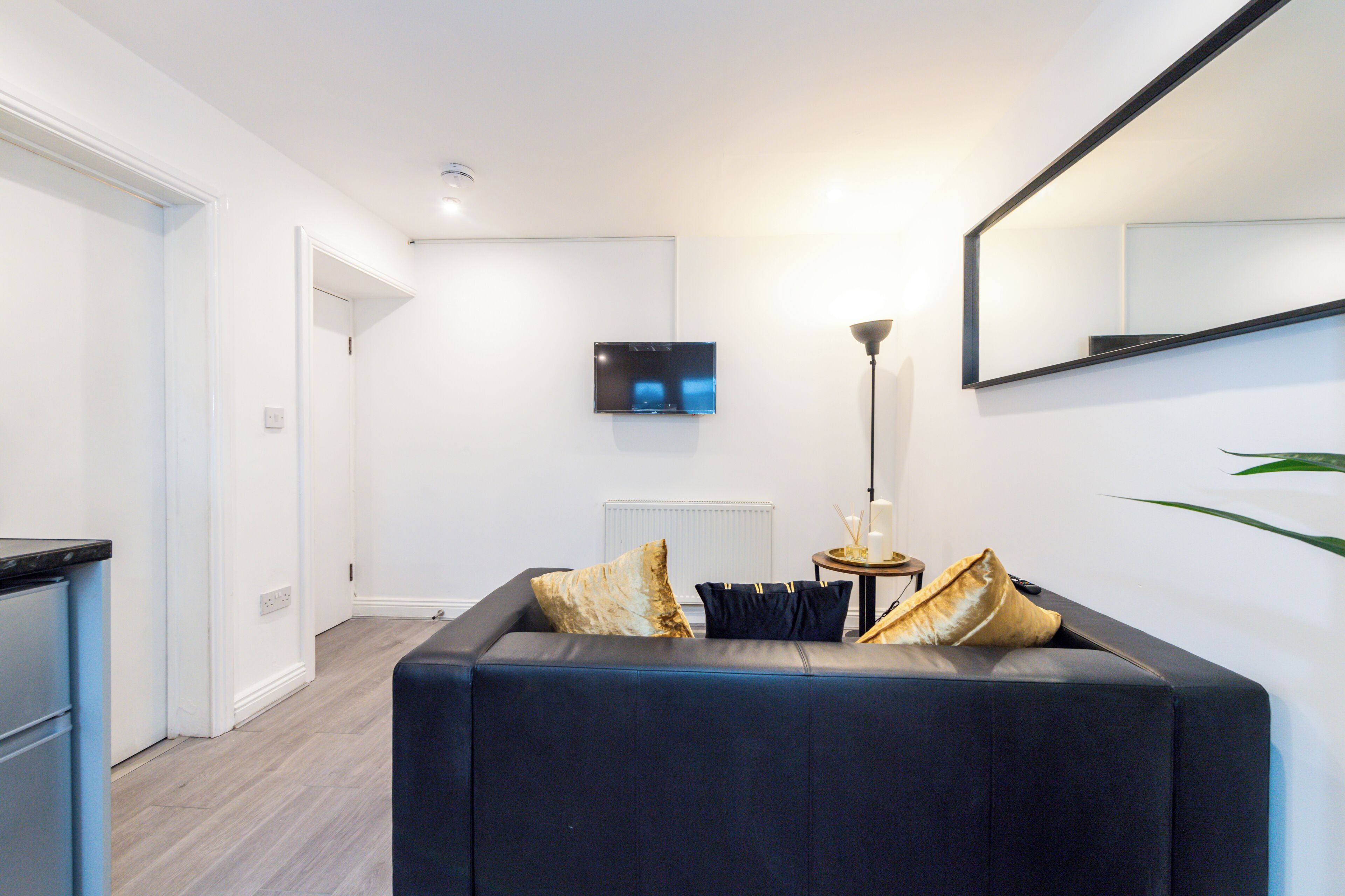 Una sala de estar moderna con un sofá oscuro, un televisor de pantalla plana montado en la pared y una lámpara de pie.