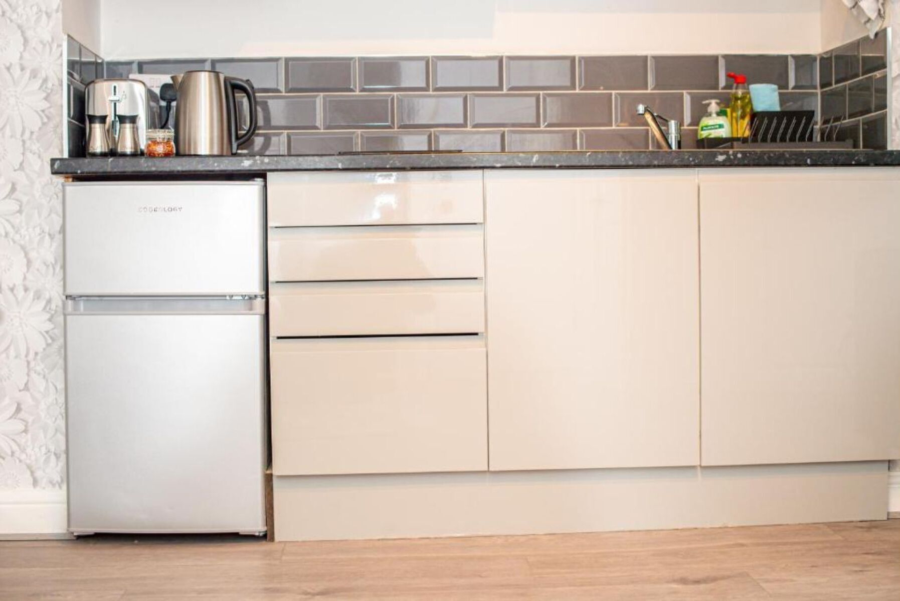 A kitchen with a refrigerator, a coffee maker, and a kettle on the countertop.