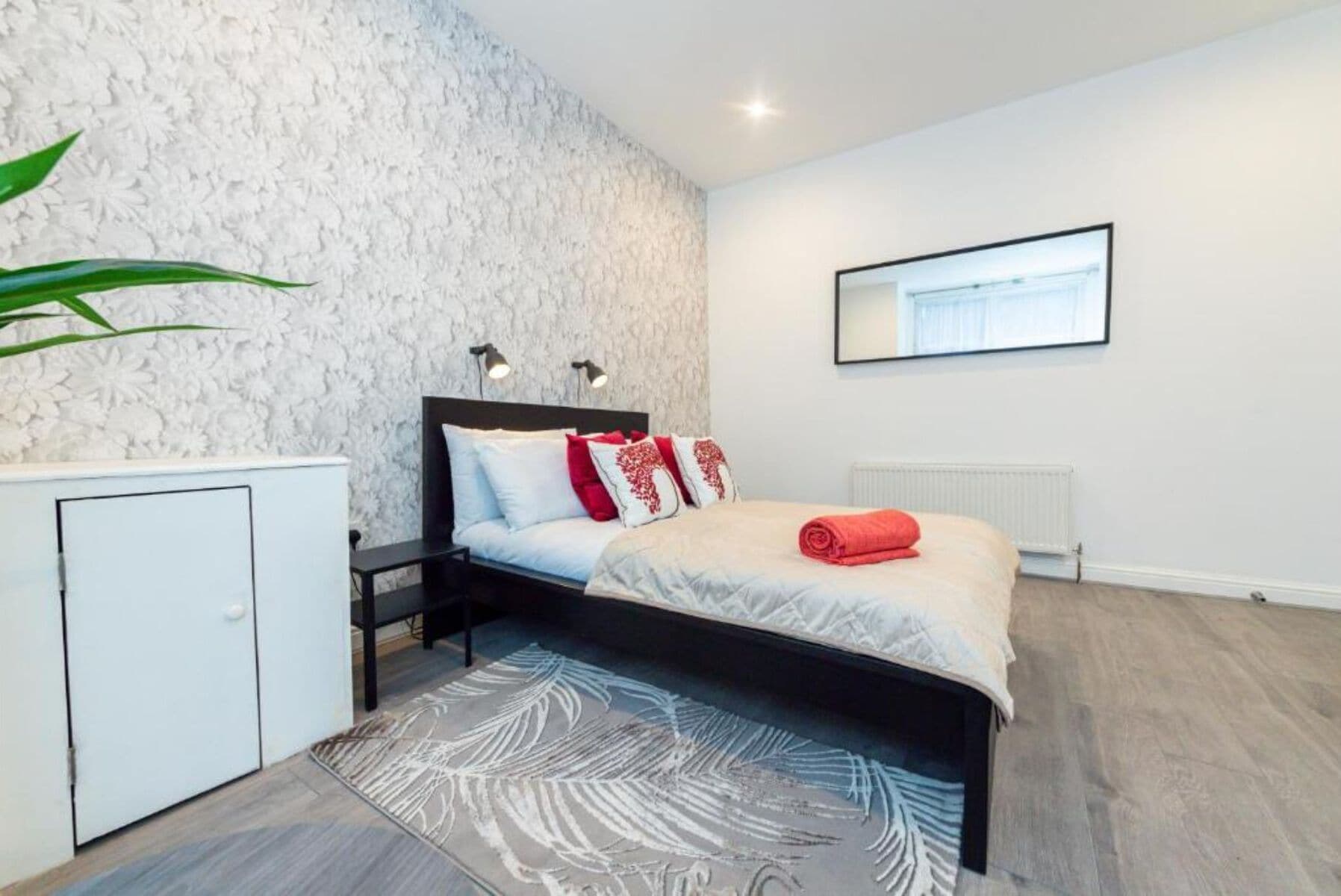 A modern bedroom with a bed, bedside tables, a radiator, and a wall-mounted TV.