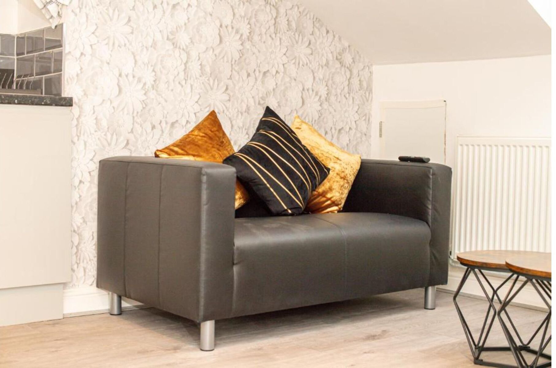 Un salon moderne avec un canapé gris, deux coussins décoratifs, une table basse en bois et un mur blanc à texture.