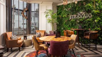 Een moderne lounge met een ronde houten tafel, lederen fauteuils en een groene wand met het bord 'The Strayaig'.