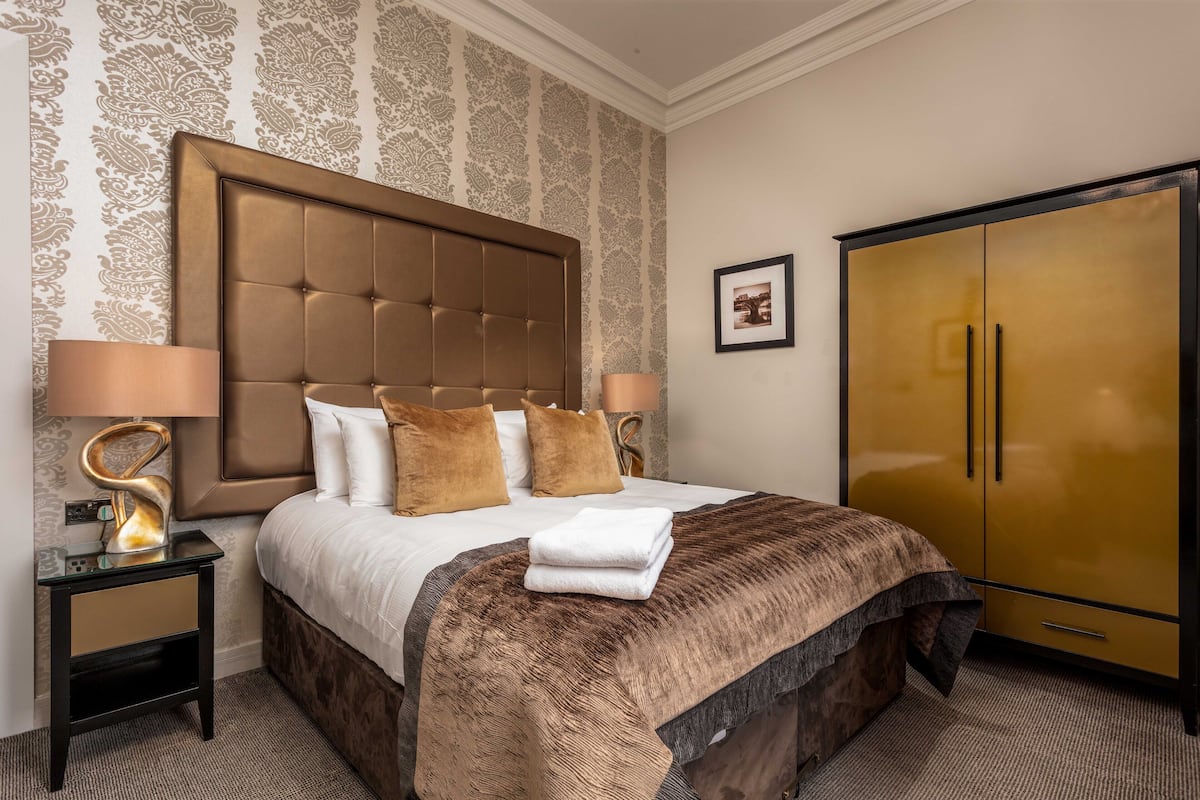 A hotel room with a large bed, two bedside tables, a wardrobe, and patterned wallpaper.