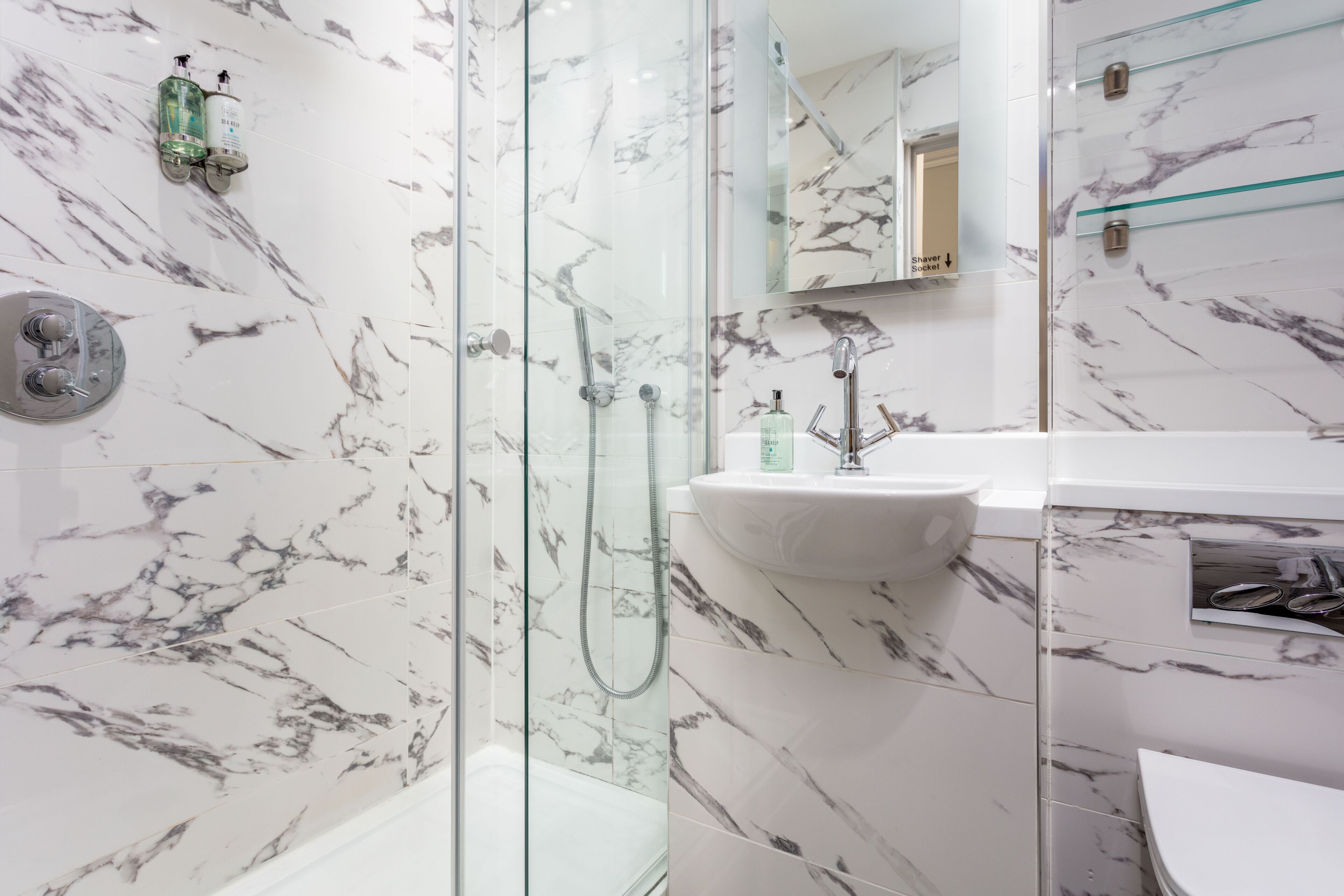 A bathroom with a glass-enclosed shower, a white sink, and marble-patterned walls.
