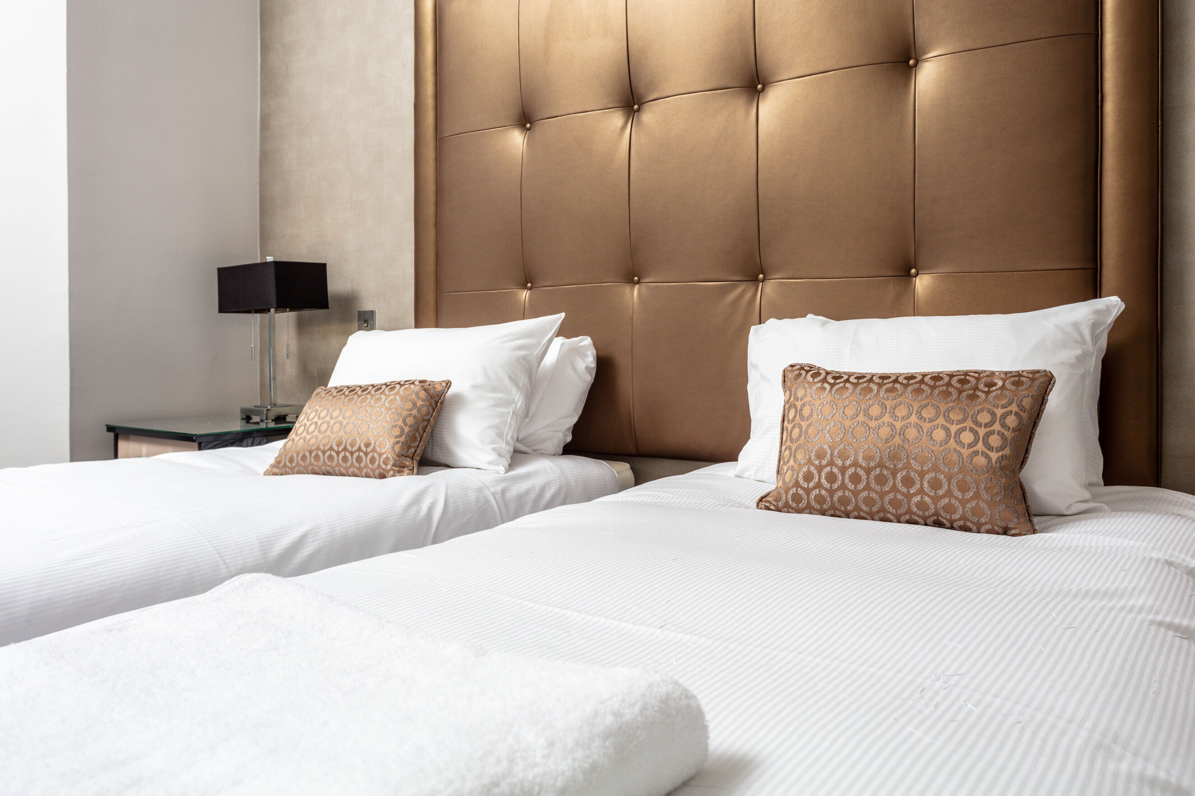 A hotel room with two beds, a tufted headboard, white linens, and patterned pillows.
