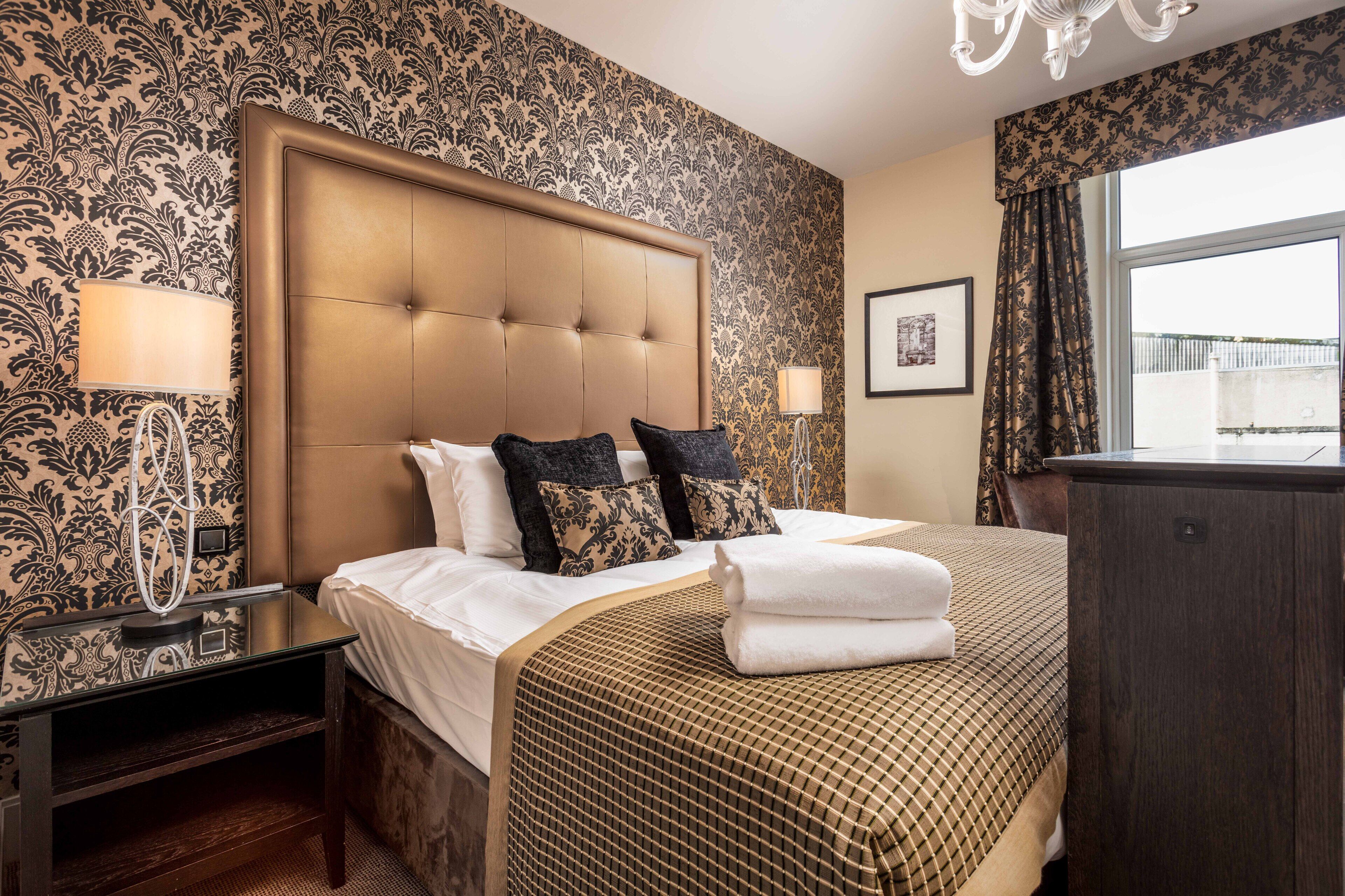 A hotel room with a large bed, two bedside lamps, a nightstand, and a view of the outside through a window.