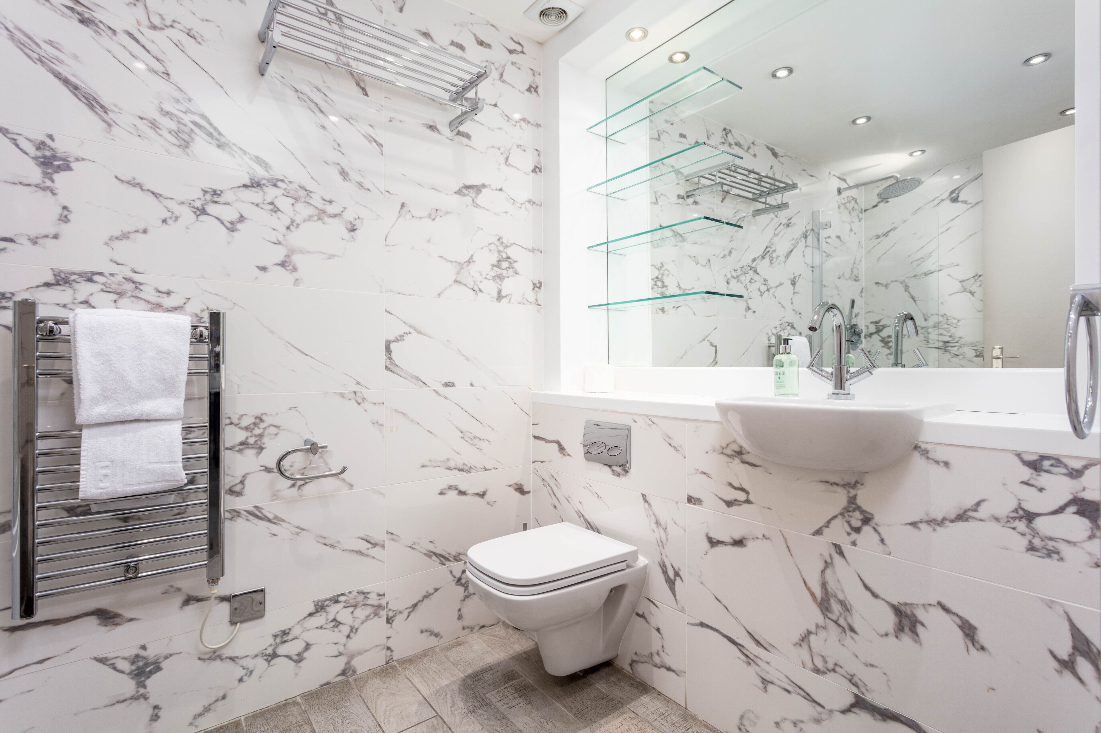 A modern bathroom with a toilet, sink, and glass shelves.