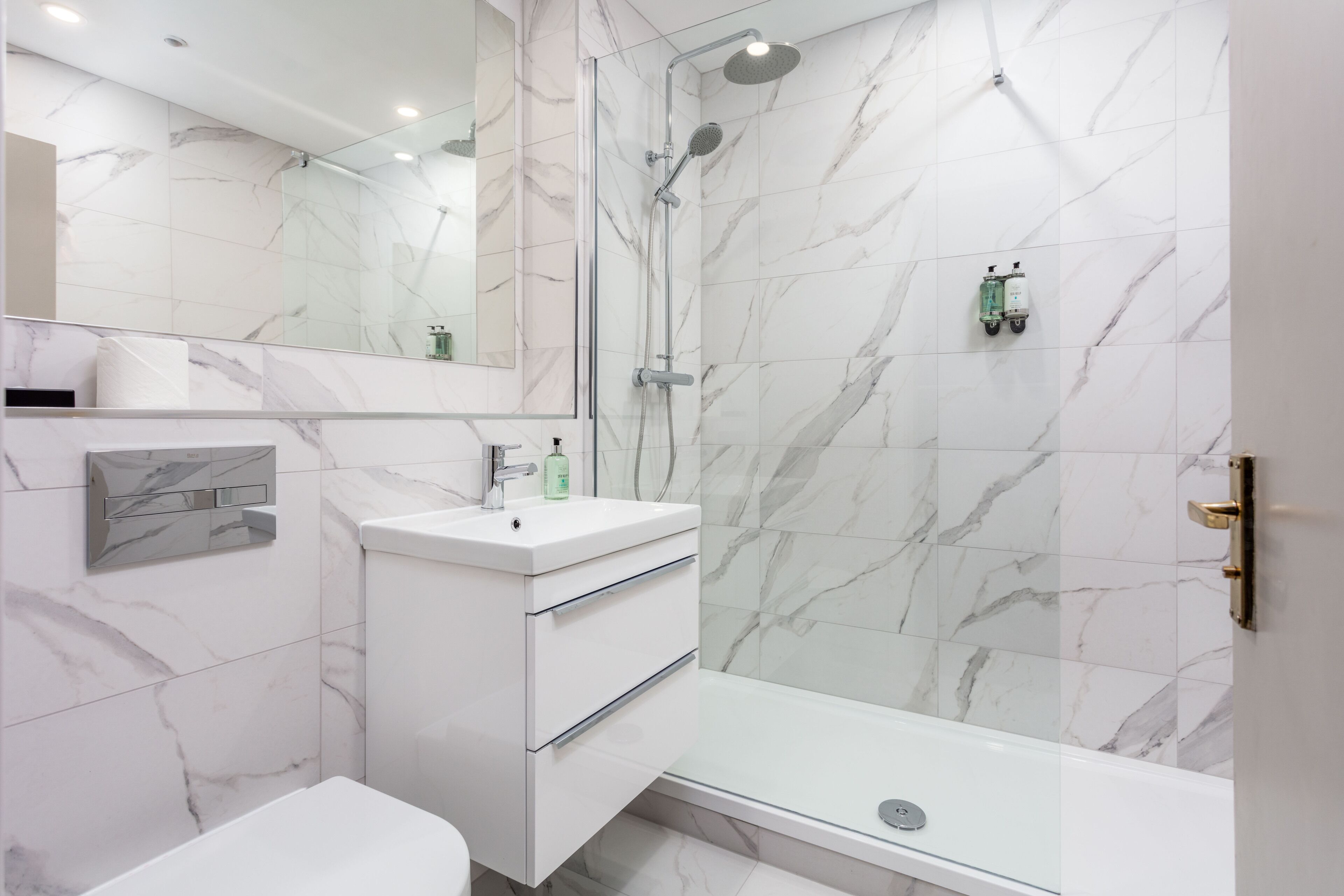 Une salle de bain moderne avec un mur en marbre, une douche en verre, un lavabo blanc et des toilettes.