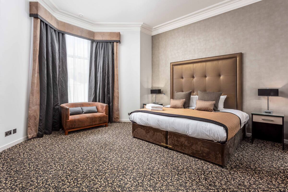 A hotel room with a large bed, a small sofa, a nightstand, and a window with curtains.