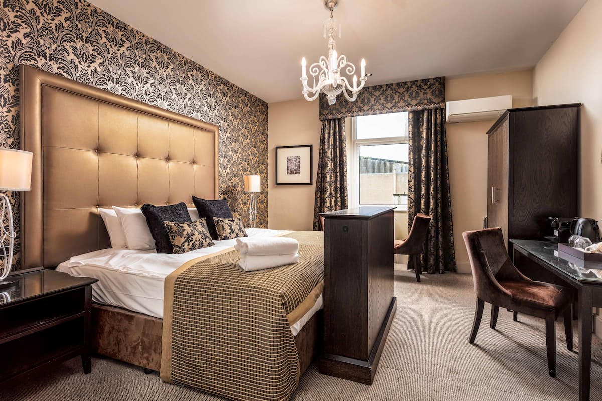 A hotel room with a large bed, a desk, a chair, a chandelier, and a view of the city through the window.
