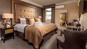 Habitación de hotel con una cama grande, una mesita de vidrio, una silla, una mesita de noche y un espejo.